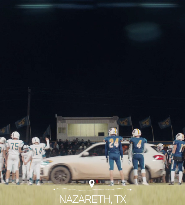 White BMW SUV on a football field surrounded by football players with "Nazareth, TX" at the bottom.